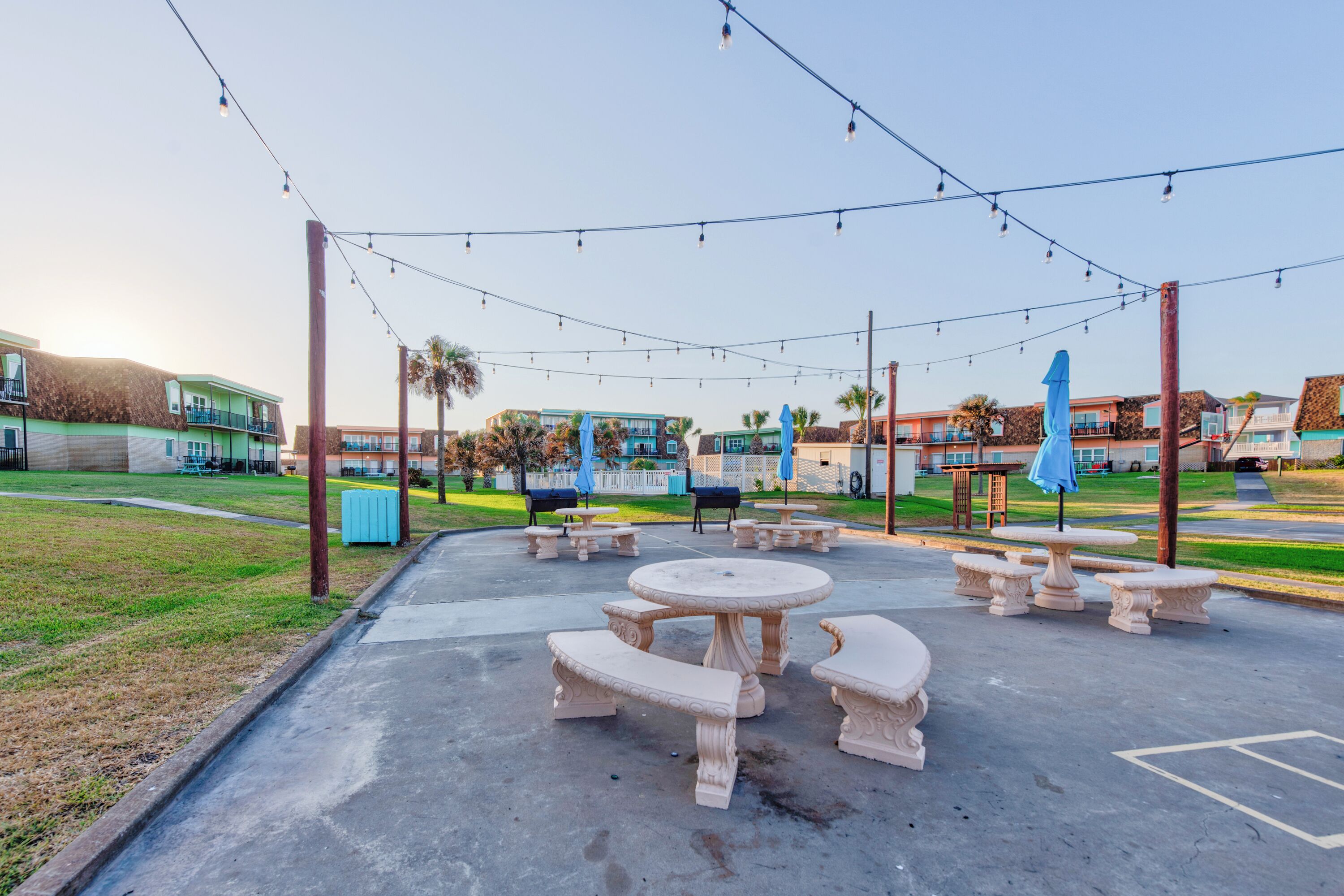 An outdoor patio area with stone tables and benches, string lights, and blue umbrellas.