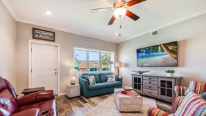 A living room with a green sofa, a red leather chair, a wooden coffee table, and a TV on the wall.