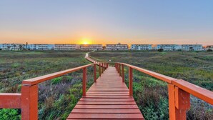 A wooden pathway leading to a row of buildings with a sunset in the background.