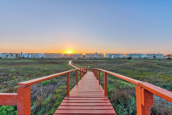 A wooden pathway leading to a row of buildings with a sunset in the background.
