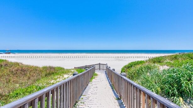 A wooden boardwalk leading to a beach with a clear blue sky.