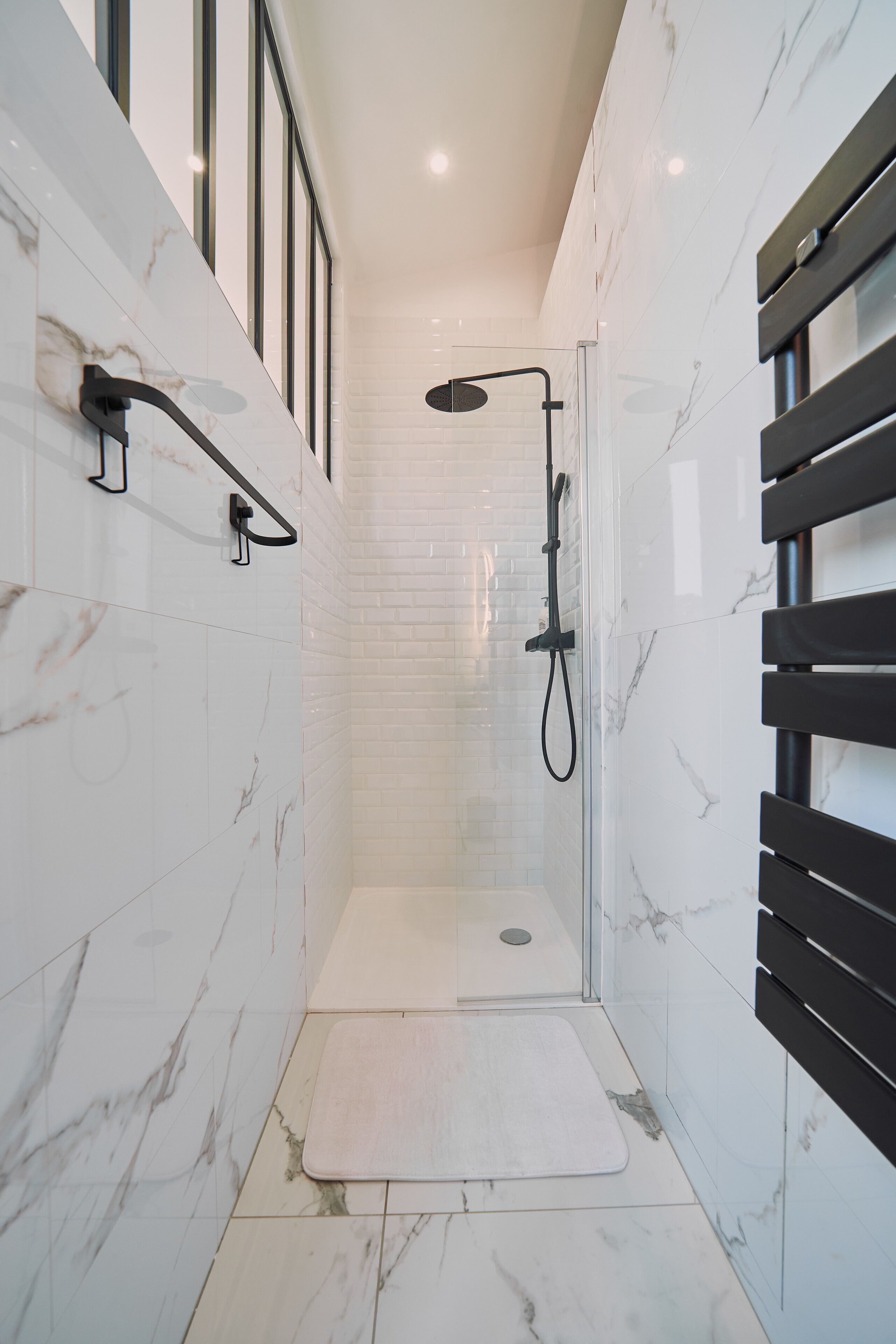 Een moderne badkamer met witte marmertegels, een douche met glazen wand en een zwarte handdoekhouder.
