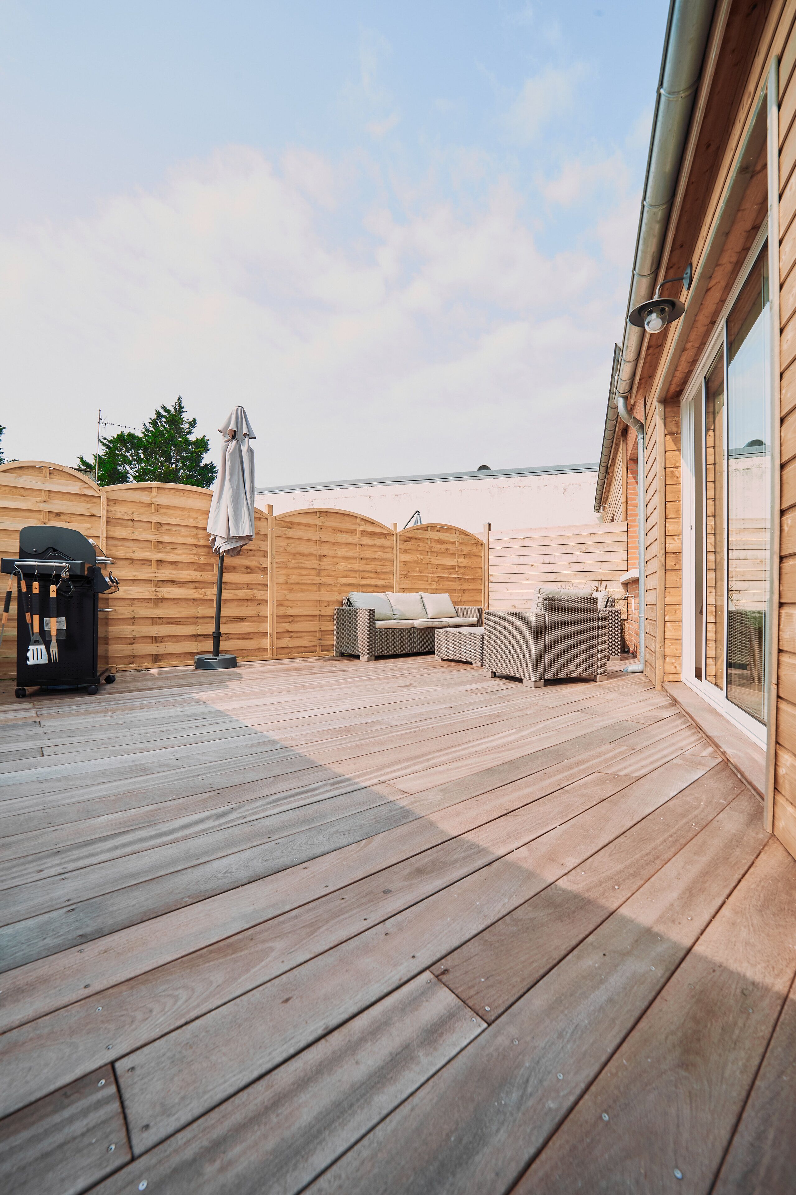 A wooden deck with outdoor furniture, a barbecue grill, and a covered umbrella.