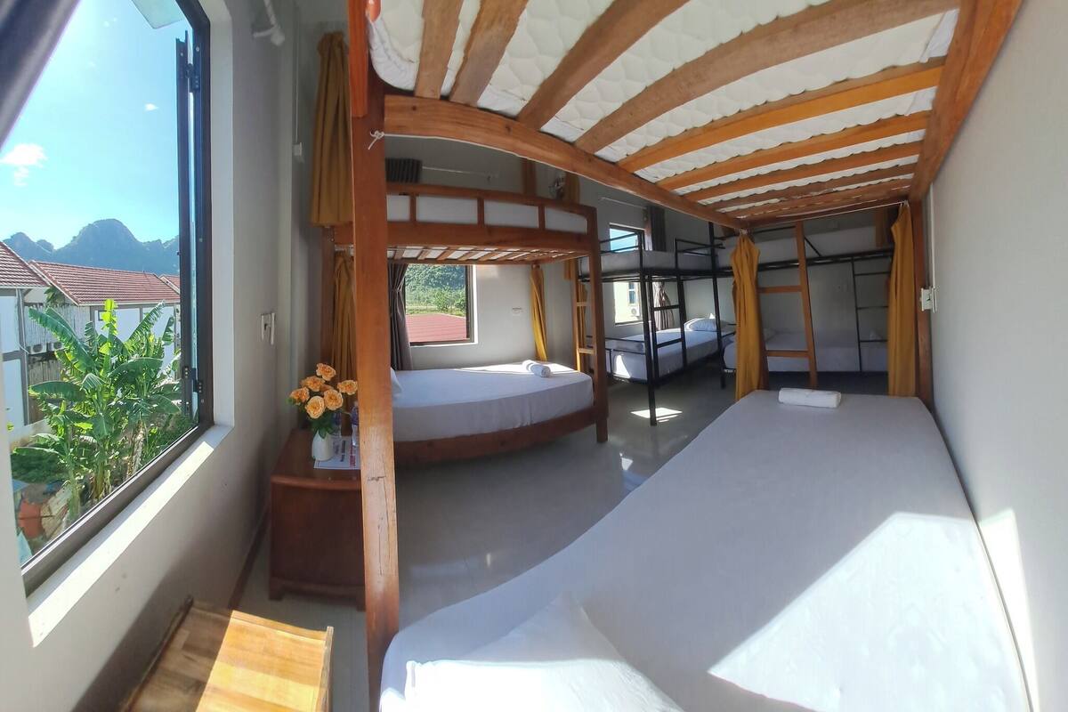 A room with bunk beds, a window with a view of mountains, and a wooden ceiling.