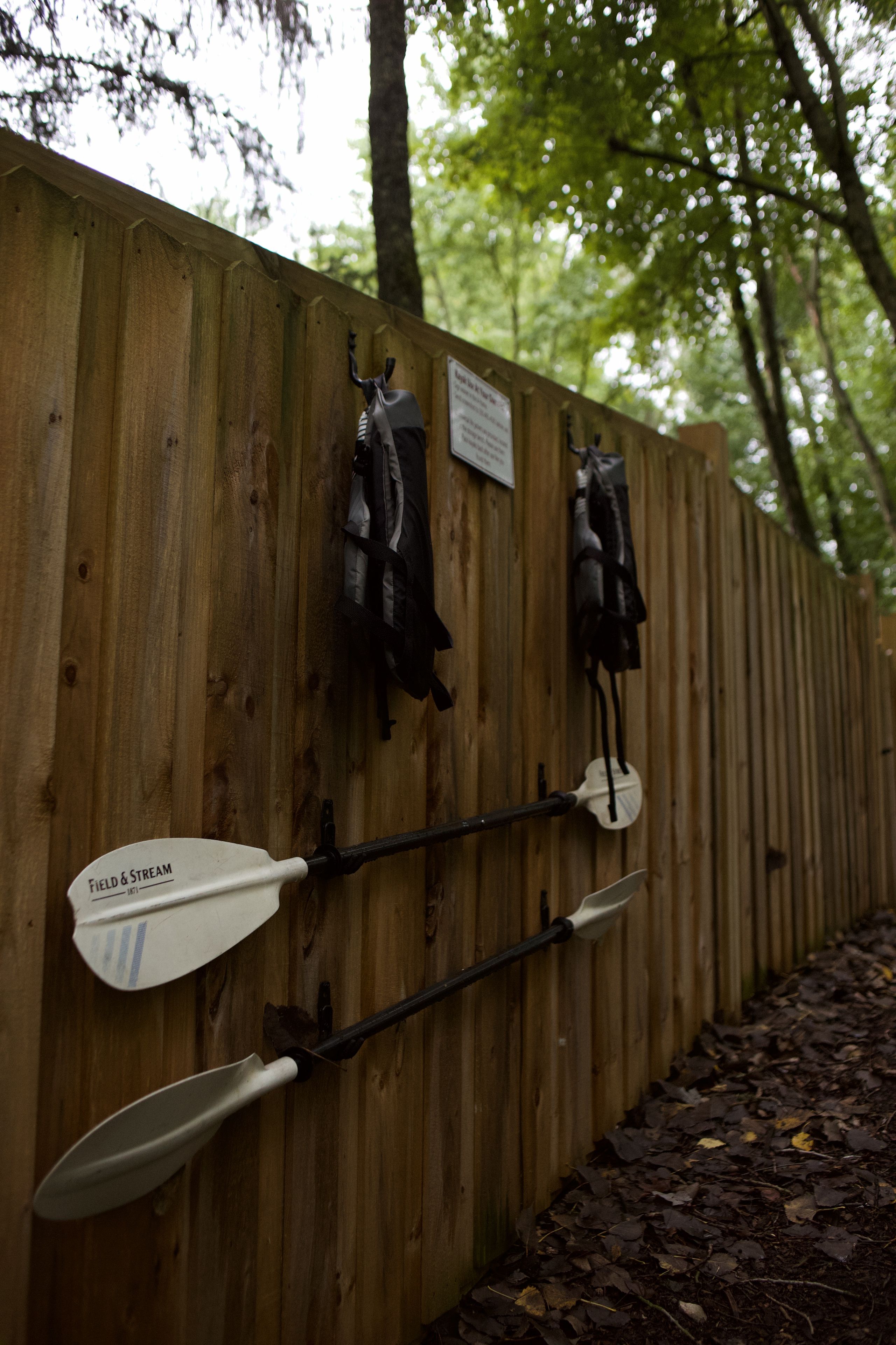 A wooden fence with two kayaks and a paddle leaning against it.
