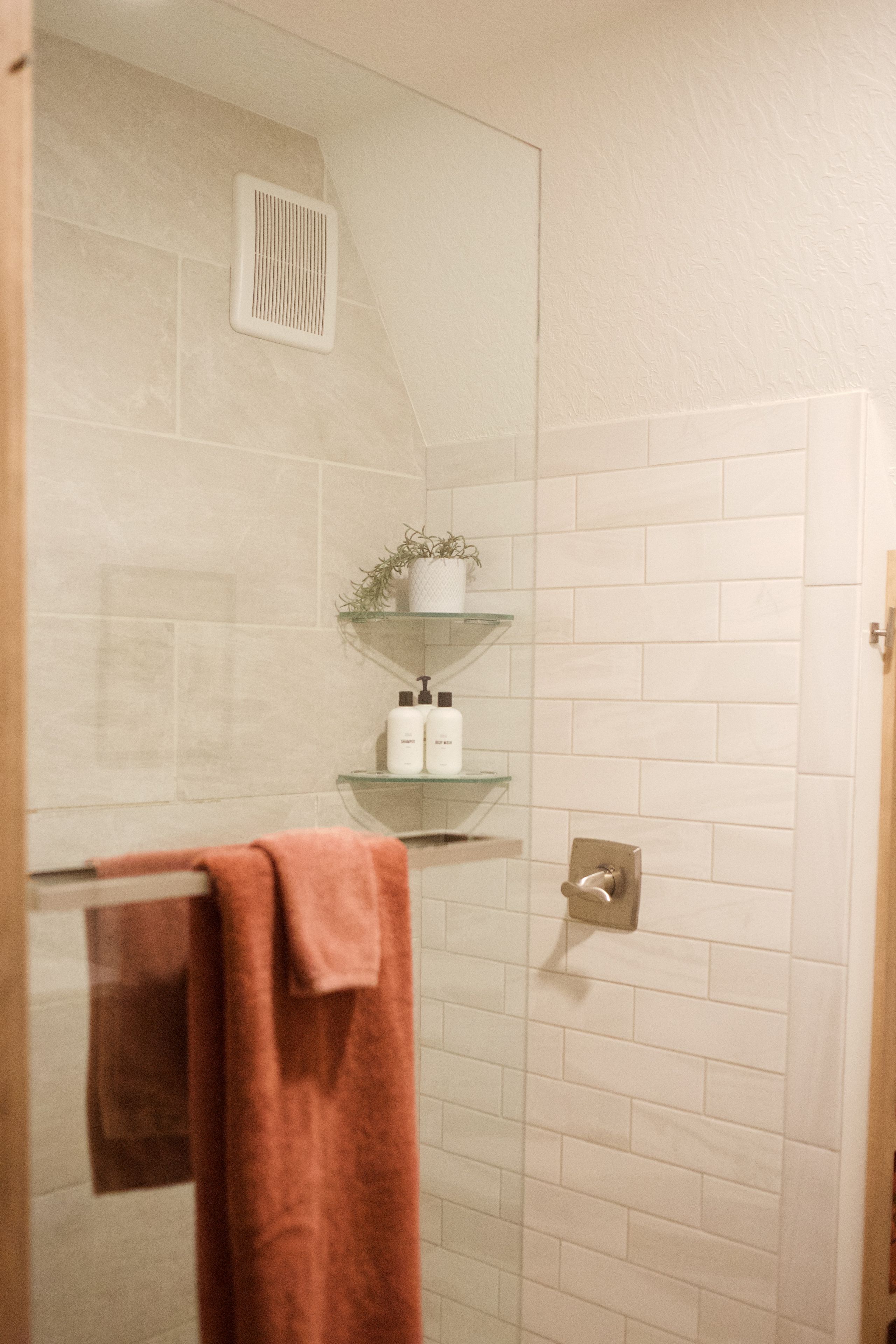 Een badkamer met een douchecabine van glas, een handdoekrek met een handdoek en een plank met toiletartikelen.