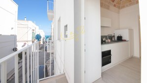 Un pasillo estrecho que conduce a un balcón con vista al mar. A la derecha se ve una zona de cocina con un fregadero y una estufa.