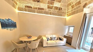 Un apartamento con dos habitaciones doble, techo de piedra, una mesa de comedor con sillas, un sofá con cojines y una mesita auxiliar.