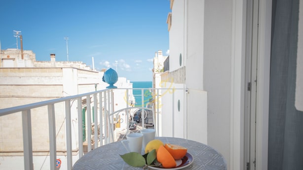 Un balcón con una mesa, un plato de fruta y vista al mar.