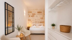 Habitación de hotel con cama, una silla, una mesita, espejo en la pared, planta en maceta y cesta de mimbre.
