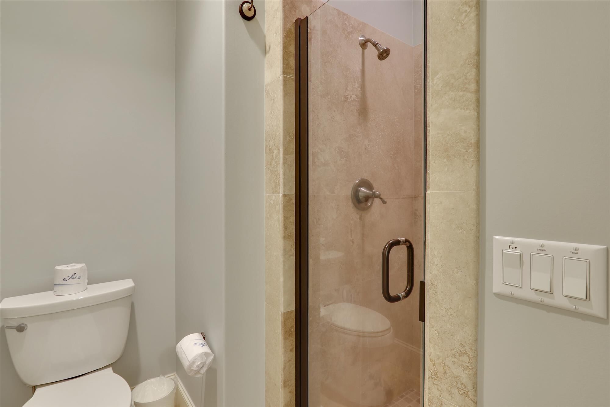 A bathroom with a toilet, a shower enclosure, and a wall-mounted light switch.