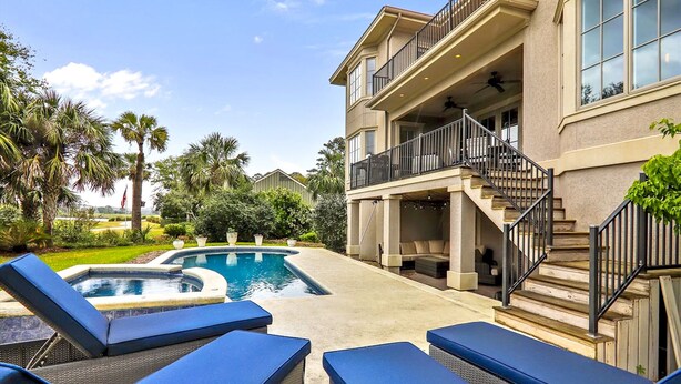 Une maison à deux étages avec une piscine, un espace salon extérieur et un balcon.