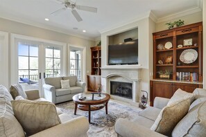 Cozy living room with a fireplace, comfortable seating, and a large window offering a view of the outdoors.