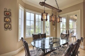 A dining area with a glass table surrounded by patterned chairs, large windows, and a rustic chandelier. - Sunset Rentals | Lookout 3 | Dog Friendly (Hilton Head Island)