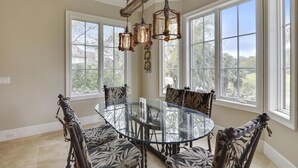 Un coin repas avec une table en verre entourée de chaises à motifs, de grandes fenêtres et un lustre de style rustique.