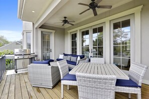 A covered outdoor patio with wicker furniture, a grill, and ceiling fans.