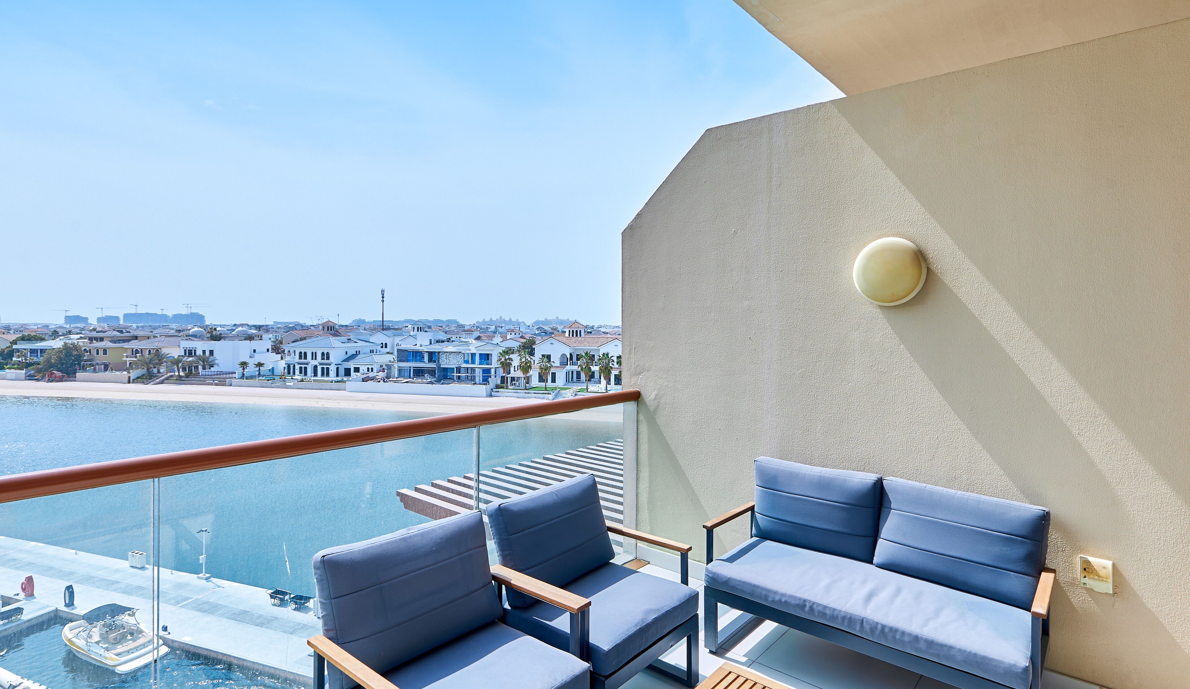 A balcony with a pool, blue chairs, and a view of a coastal town.
