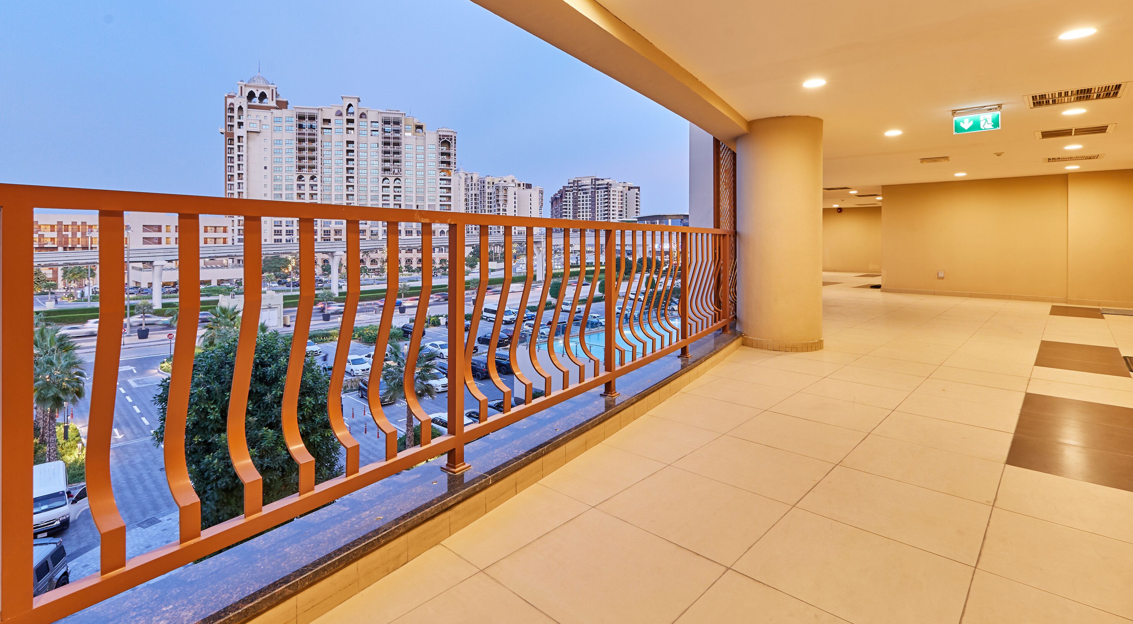 A hotel corridor with a view of a cityscape, including high-rise buildings and a parking area.