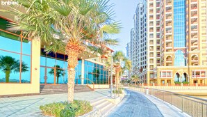 A modern hotel with a glass facade, palm trees, and a cobblestone pathway. - bnbme | Palm Views West | STUDIO (Dubai)