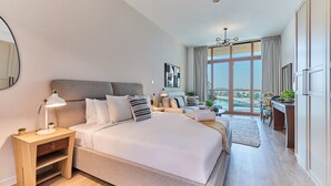 A modern hotel room with a large bed, a desk, and a view of a body of water. - bnbme | Palm Views West | STUDIO (Dubai)