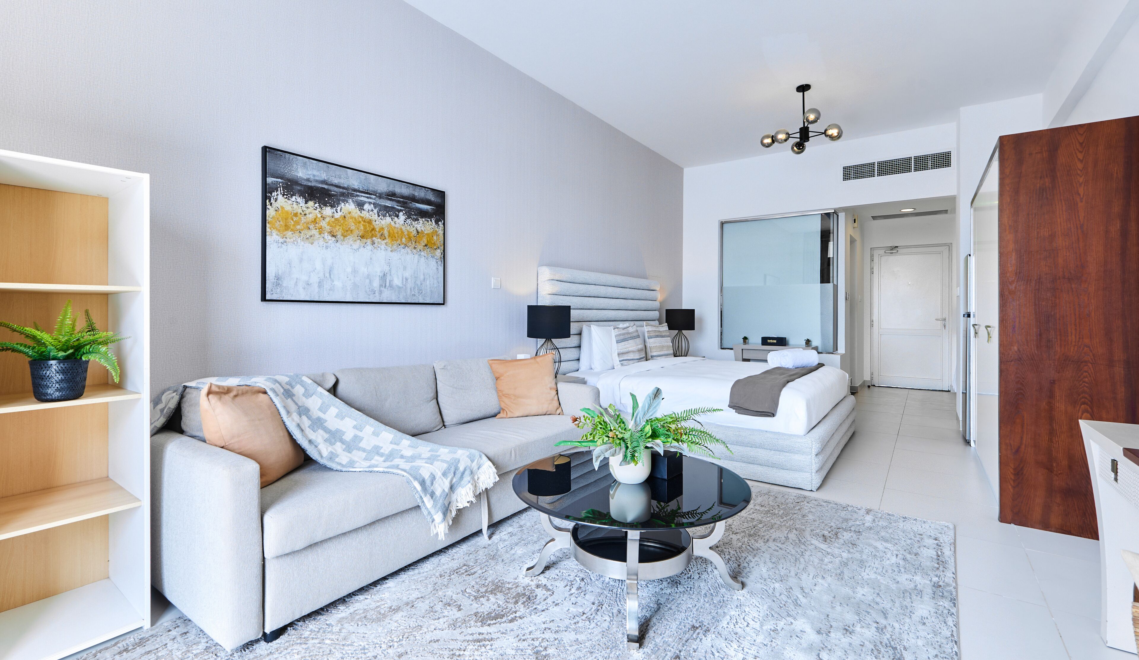 Une chambre d’hôtel moderne, dotée d’un canapé, d’une table basse ronde, d’un lit avec une tête de lit, d’un grand miroir et d’un luminaire au plafond.