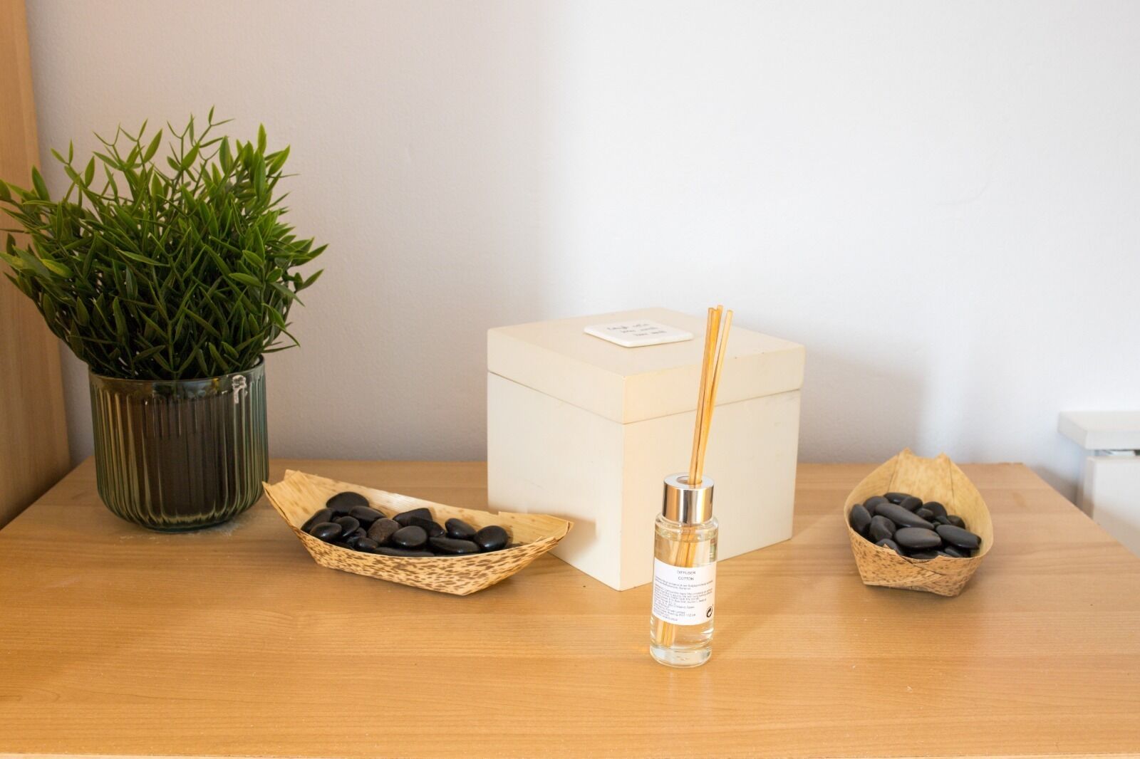 A wooden table with a potted plant, a diffuser, and two bowls of stones.