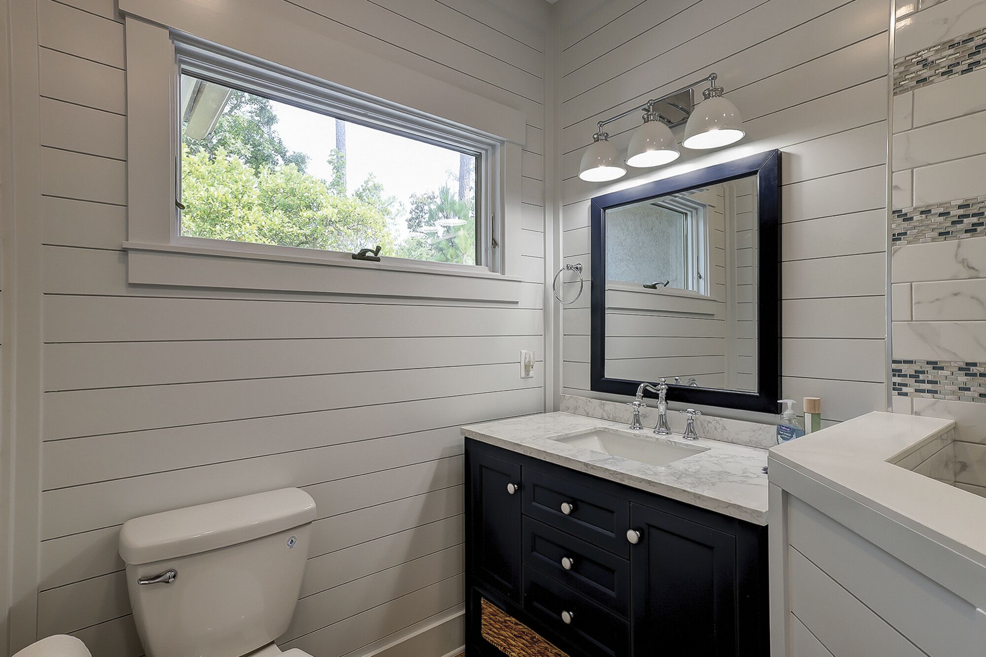 Ein Badezimmer mit Fenster, Waschbecken, Spiegel und Toilette.