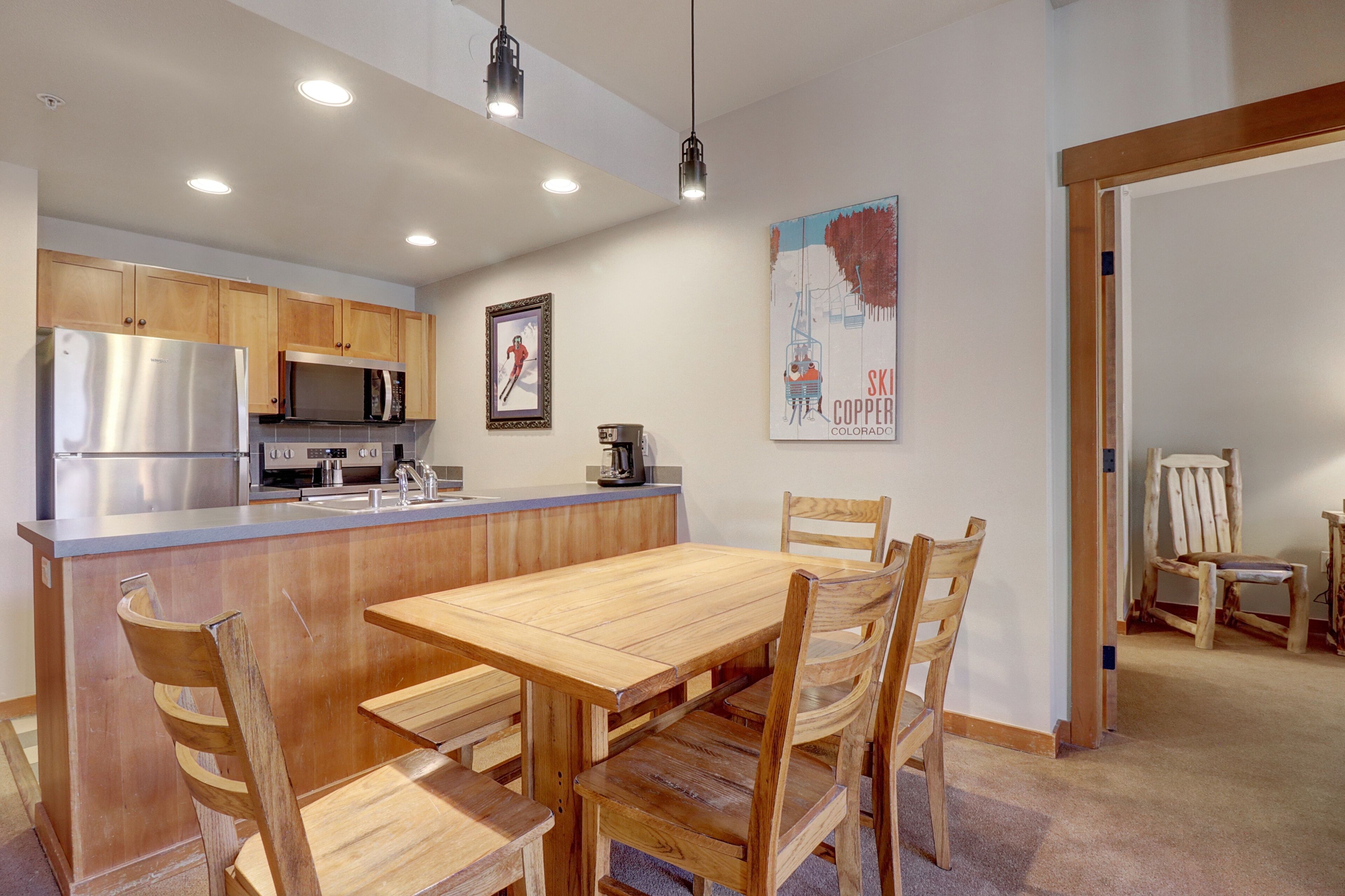 A modern kitchen with wooden cabinets, stainless steel appliances, and a wooden dining table with chairs.
