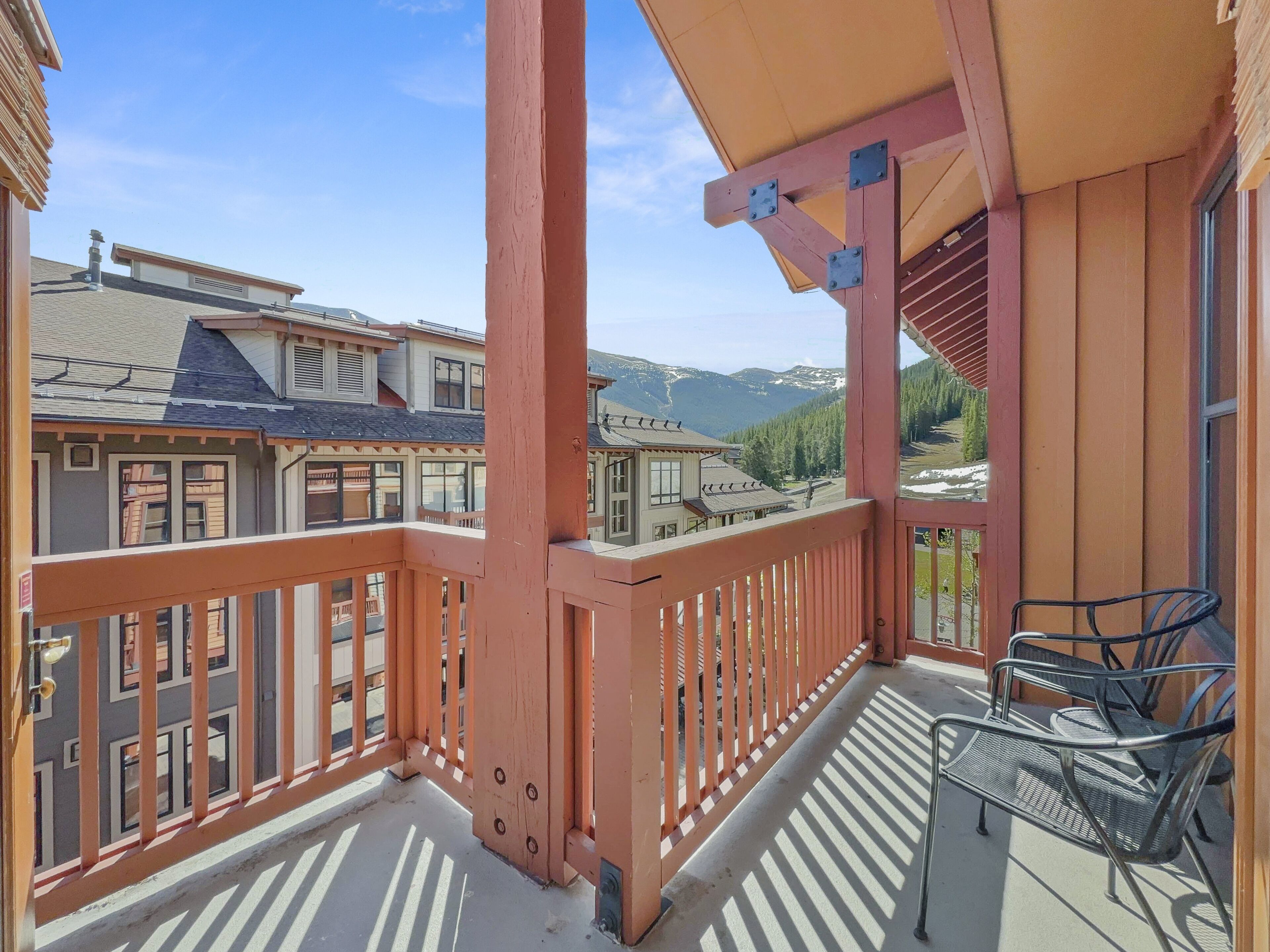 A balcony with a view of a mountain landscape, a wooden railing, and two metal chairs.