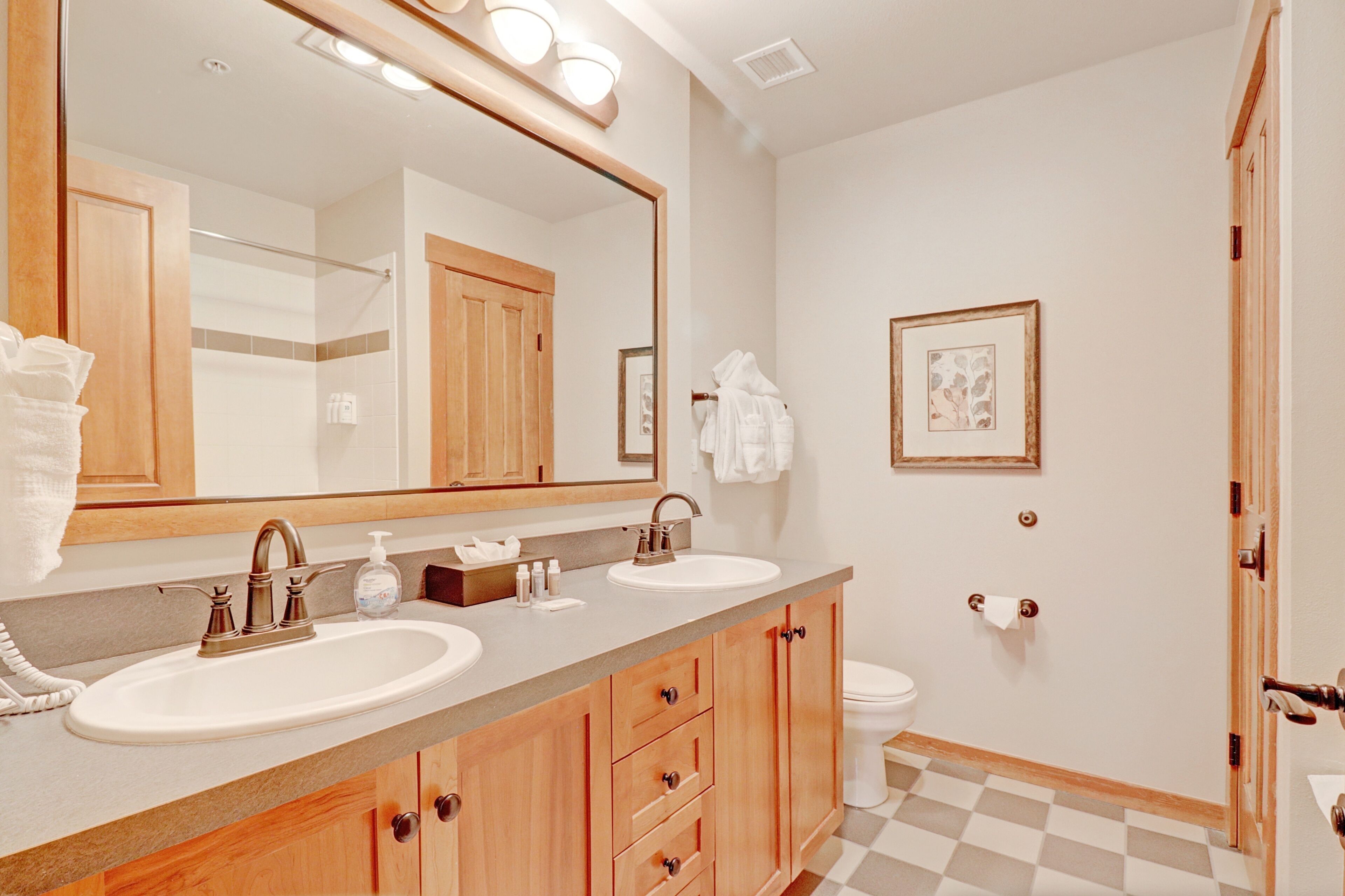 A bathroom with two sinks, a large mirror, wooden cabinets, a toilet, and a shower area.