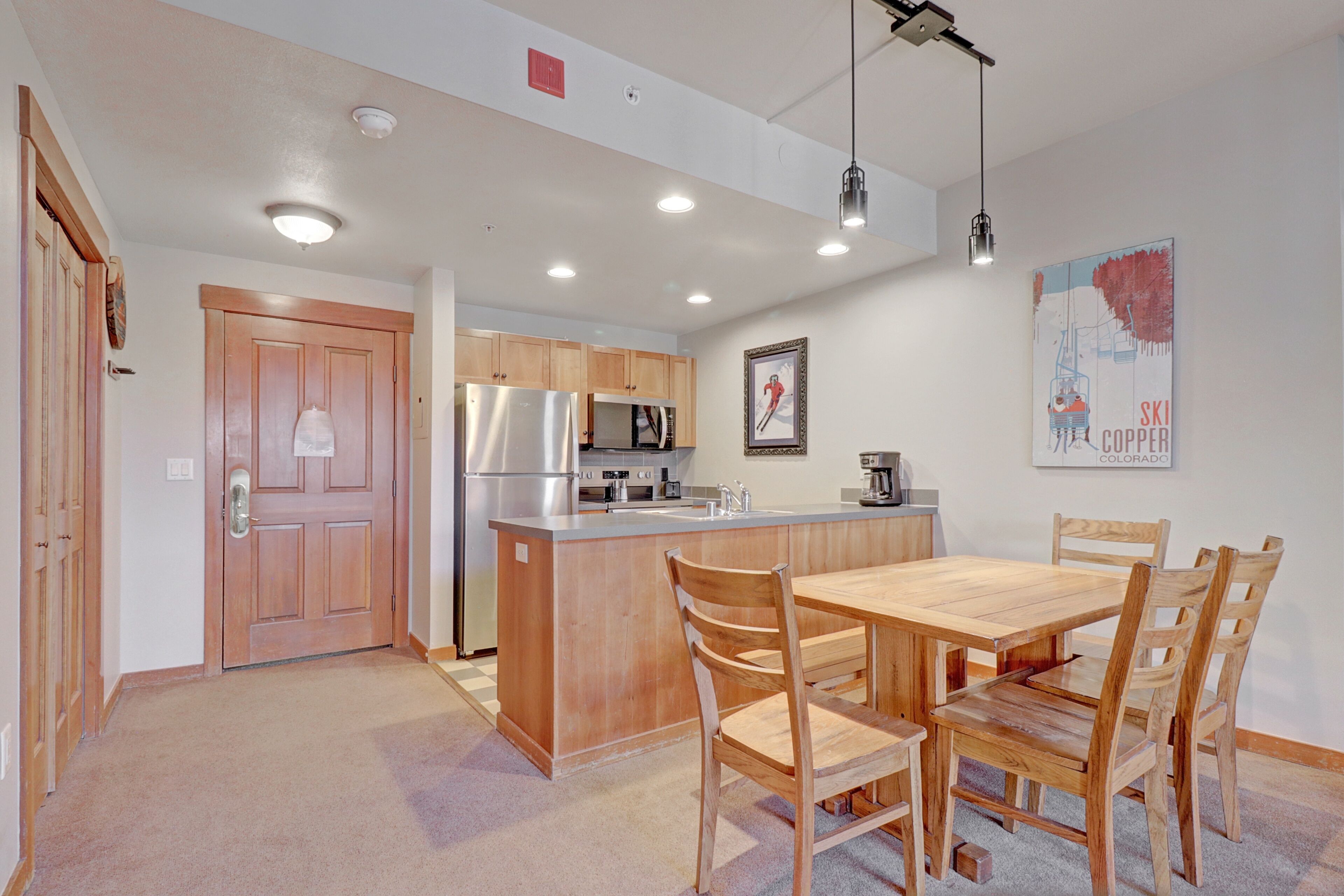 A modern kitchen with wooden cabinets, a stainless steel refrigerator, and a wooden dining table with chairs.