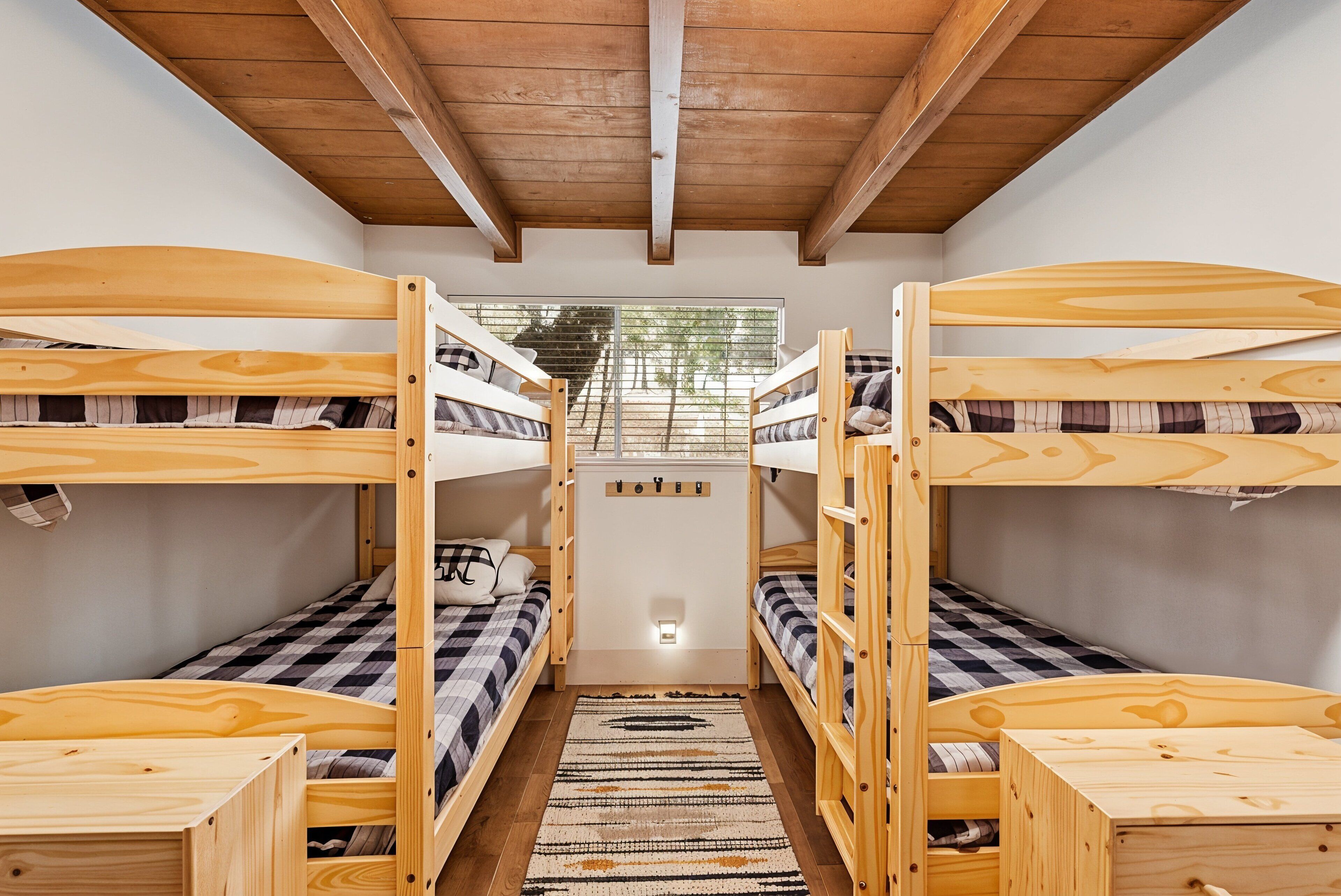 A room with three bunk beds arranged in a row, wooden headboards, a checkered bedspread, and a patterned rug on the floor.