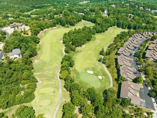 Vue aérienne d’un terrain de golf avec un club-house, entouré de logements résidentiels et d’une végétation luxuriante.