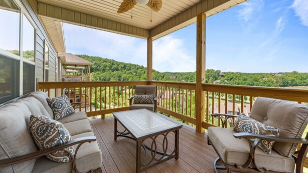 A covered outdoor deck with a sofa, chairs, and a table, overlooking a green landscape. - Tee House At Stonebridge 3 Bedroom Condo by RedAwning (Branson West)