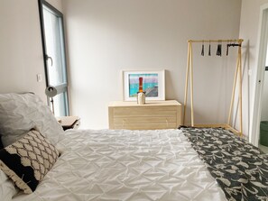 A bedroom with a bed, a nightstand, a framed picture, and a wooden hanger stand. - Beautiful Architect-Designed House, Kérity (Penmarc'h)