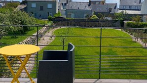 Eine Terrasse mit einem gelben Tisch und einem schwarzen Stuhl, mit Blick auf einen gepflegten Rasen und Häuser im Hintergrund.