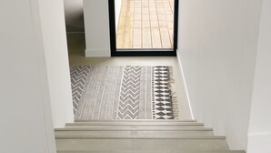 Eine Treppe mit einem gemusterten Teppich, der zu einer Tür führt, welche in einen Garten hinein öffnet.