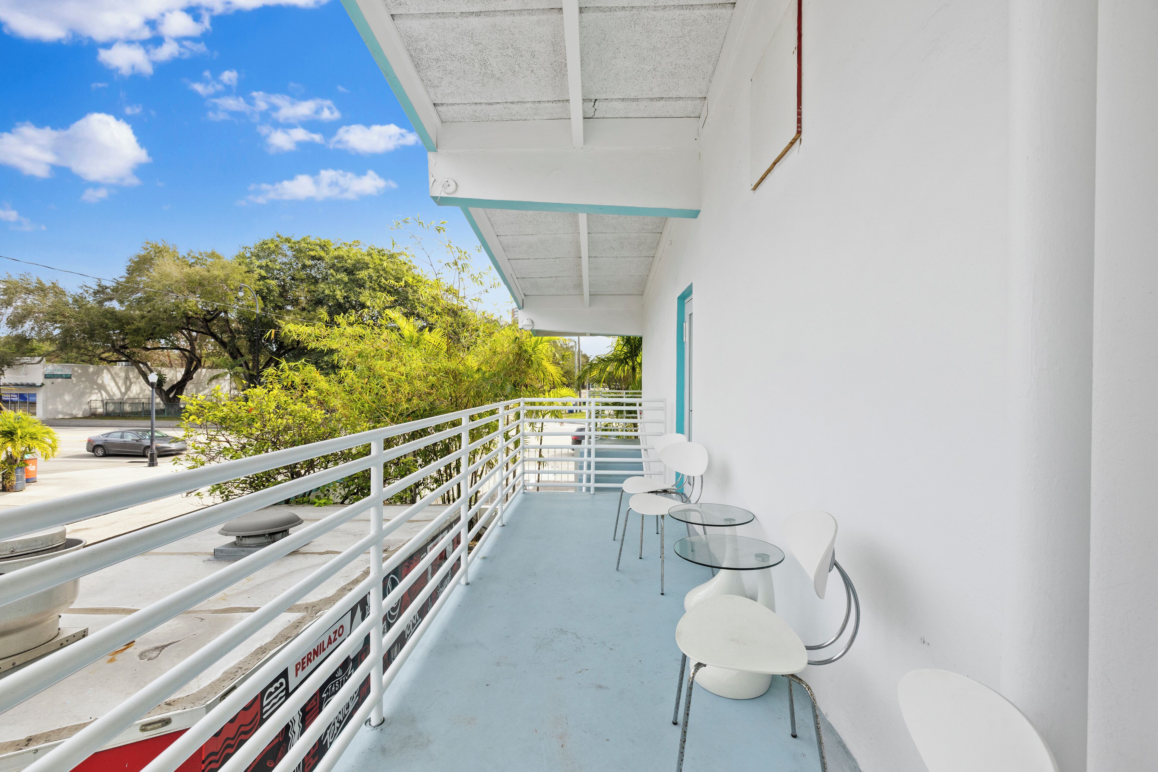 Un balcon avec des balustrades blanches, une table en verre et des chaises blanches.