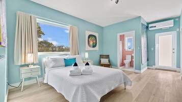 Una camera da letto con un letto grande, una finestra, un comodino, un tavolino di servizio, un quadro, un bagno con il water e un condizionatore d'aria.