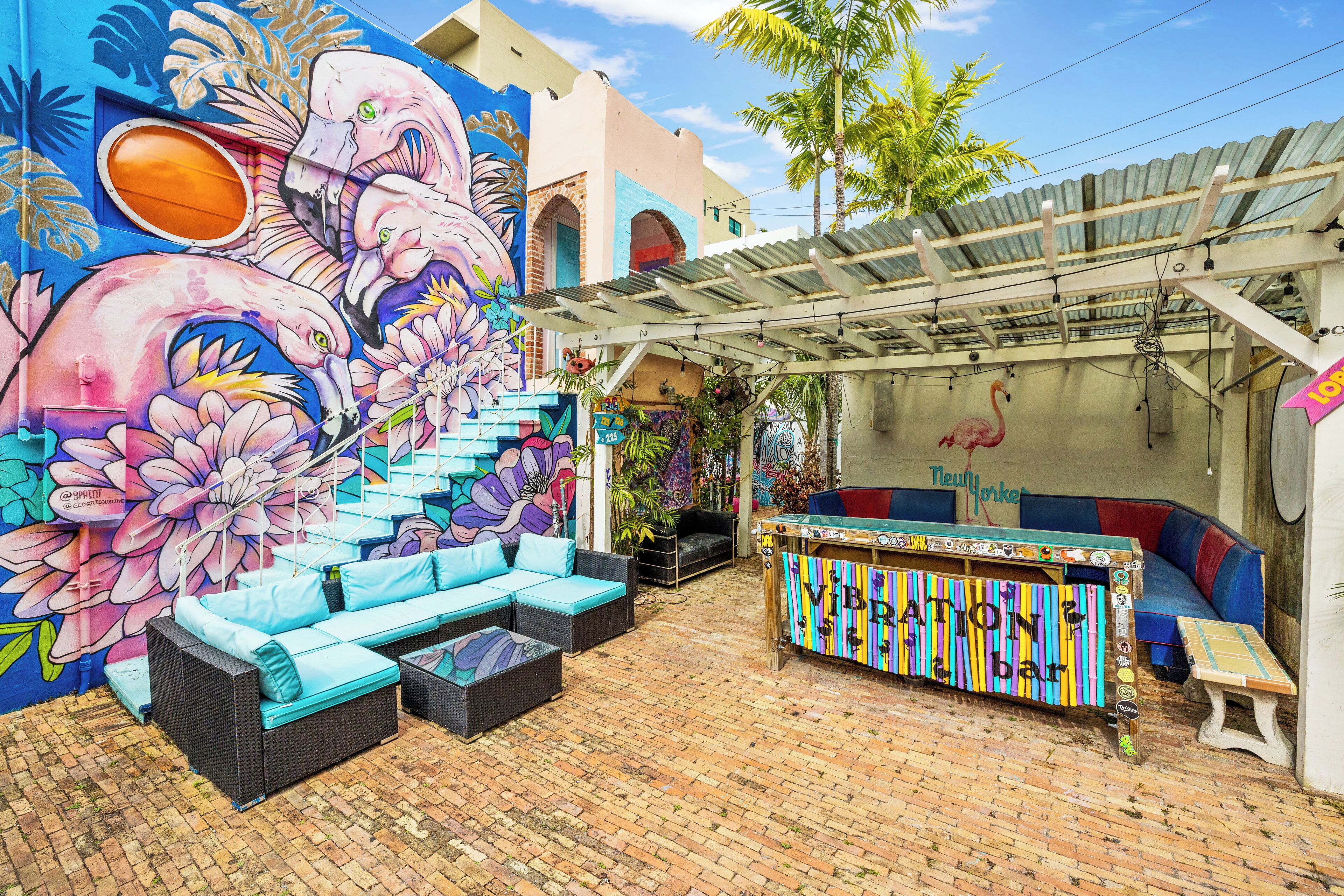Una zona d'estar a l'aire lliure vibrant, amb un mural colorit, un bar tiki i una escala que condueix a una planta superior.