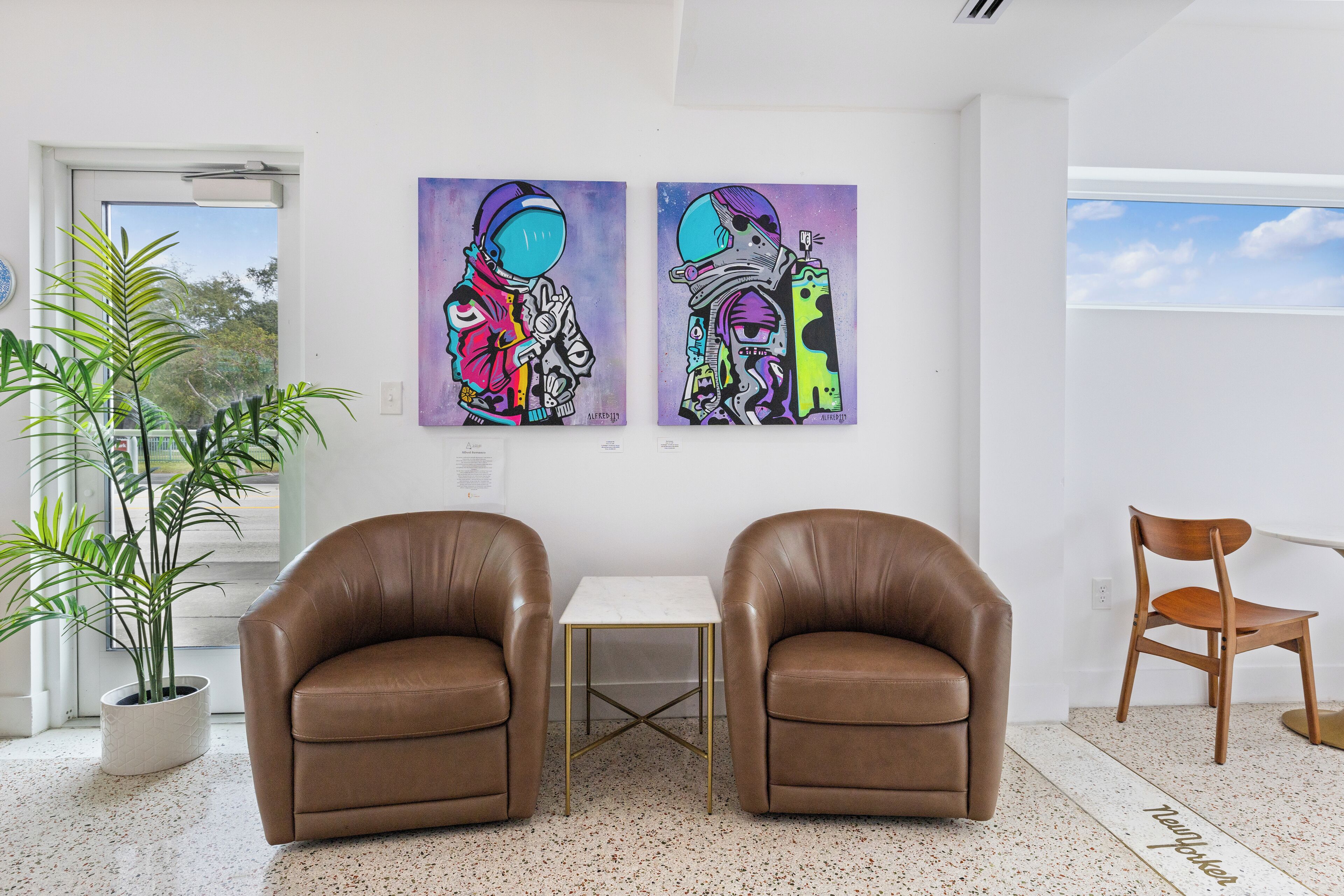 A room with two brown leather chairs, a small white table, and two abstract paintings on the wall.