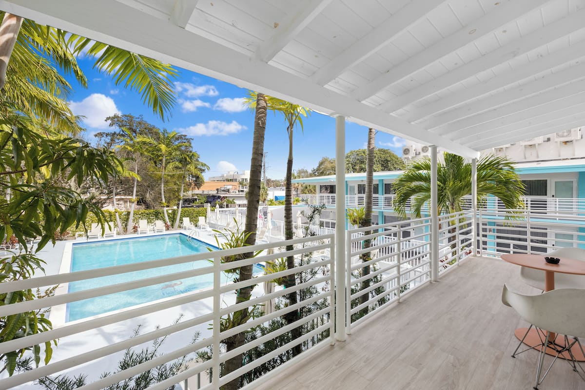A balcony with a pool, palm trees, and a view of a building.