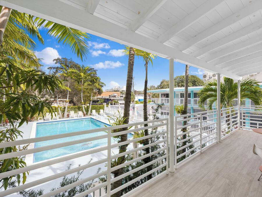 Un balcone con piscina, palme e vista su un edificio.