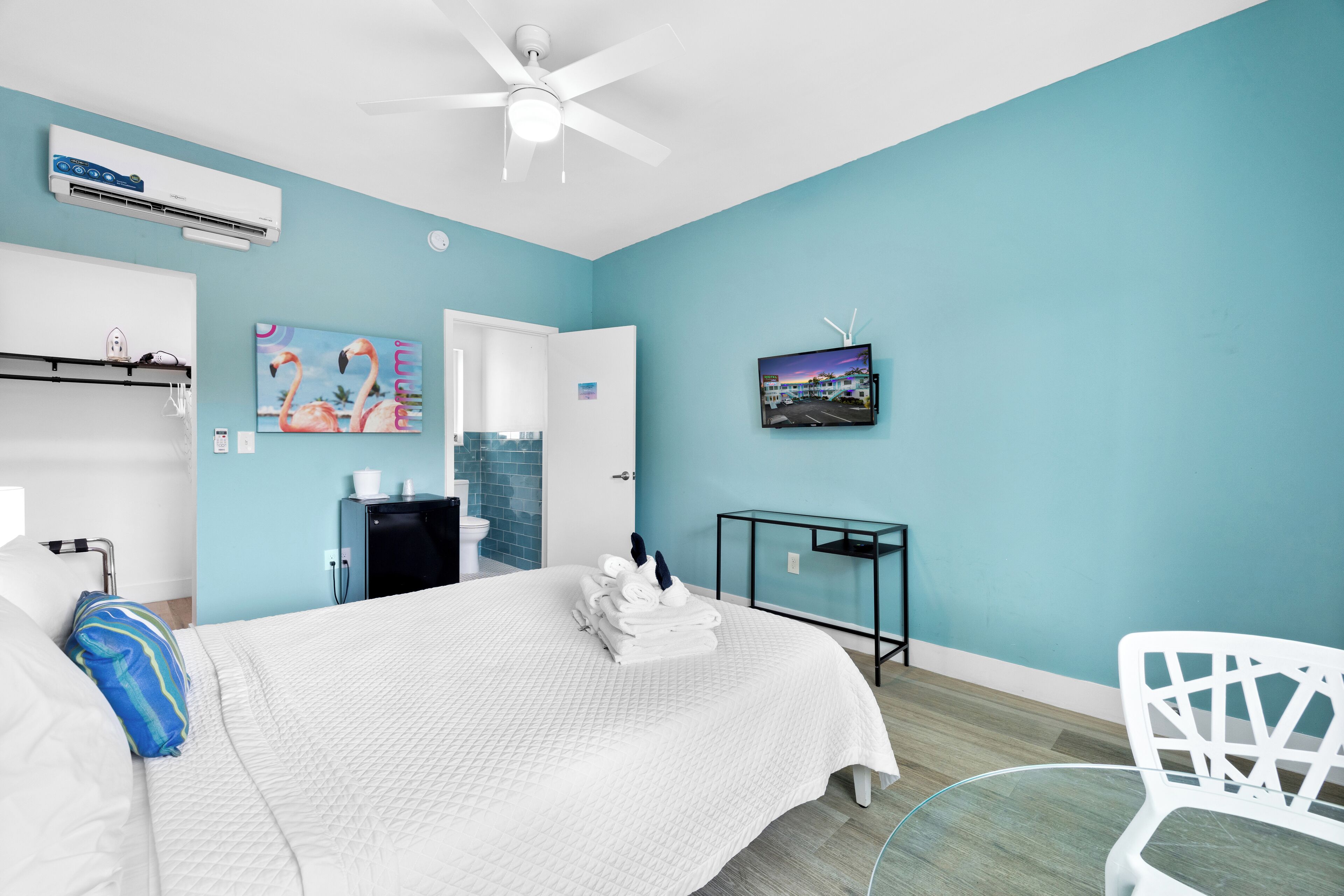 A modern hotel room with a bed, a desk, a chair, and a TV on the wall.