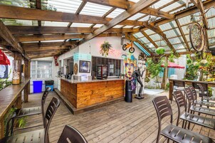 Un caffè all'aperto con tavoli e sedie in legno, un'area bar con insegna al neon e un soffitto rustico in legno.