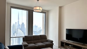 A modern living room with a large window, a sofa, a coffee table, and a TV on a wooden stand. - Lux BnB Amna Tower Burj Views (Dubai)