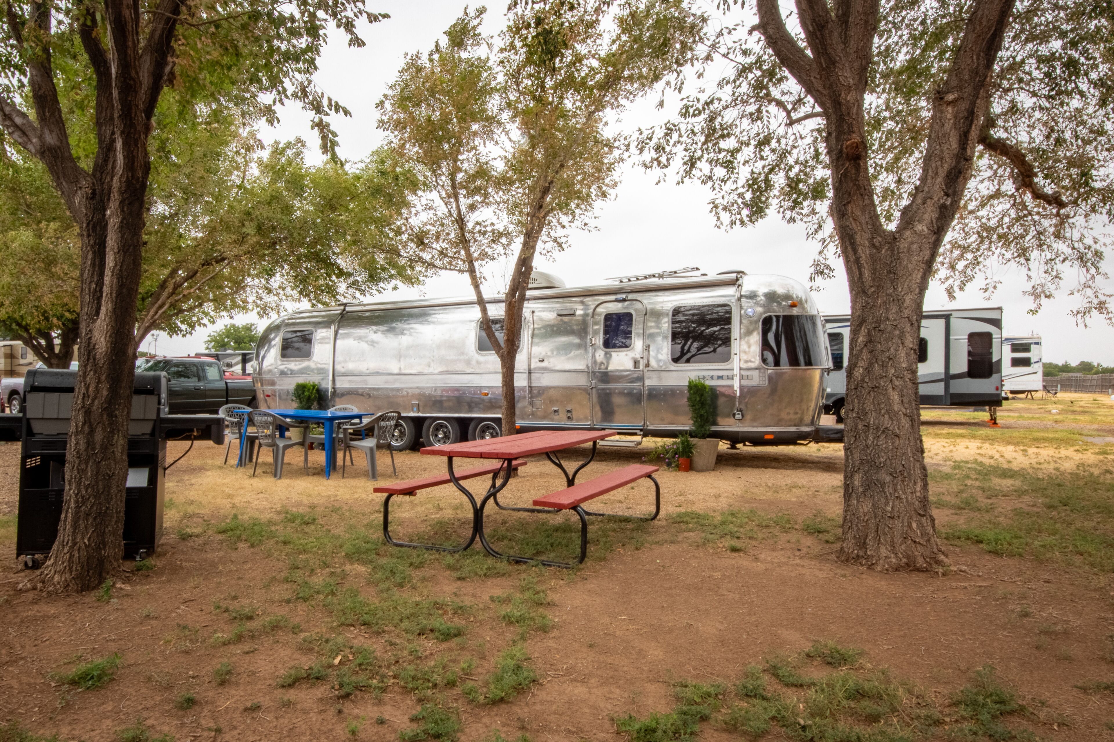 A campsite with a picnic table and chairs, surrounded by trees and a trailer.