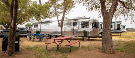 A campsite with a picnic table and chairs, surrounded by trees and a trailer.
