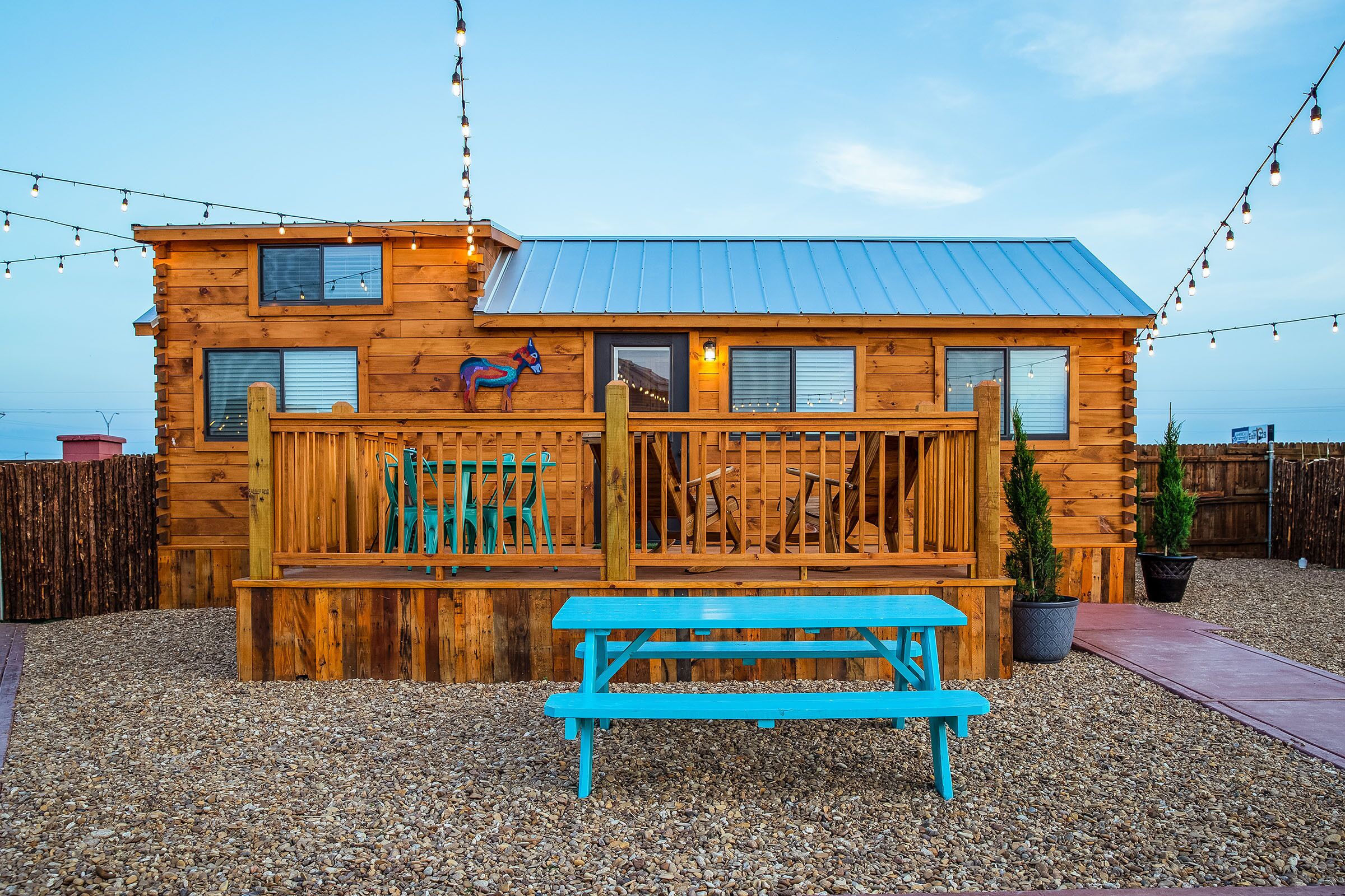 A wooden cabin with a deck, a bench, and string lights.