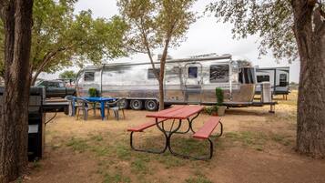 Un terrain de camping équipé d’une table et de chaises pour pique-nique, d’une remorque et d’un camion.